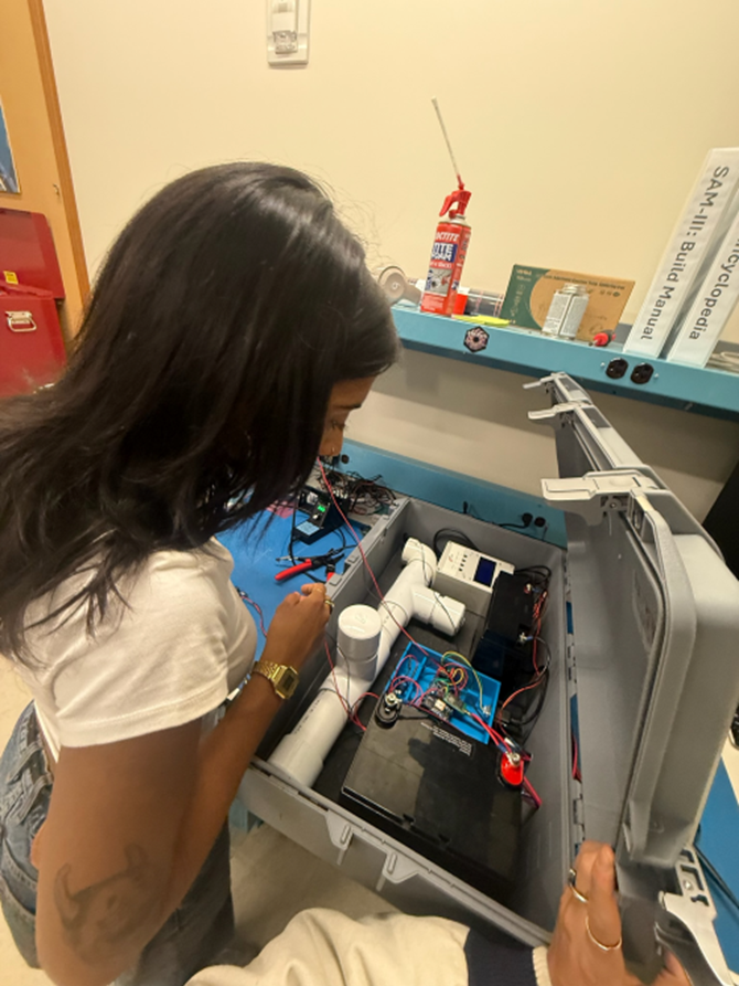 A person with long black hair looking over a set of equipment in a closable box