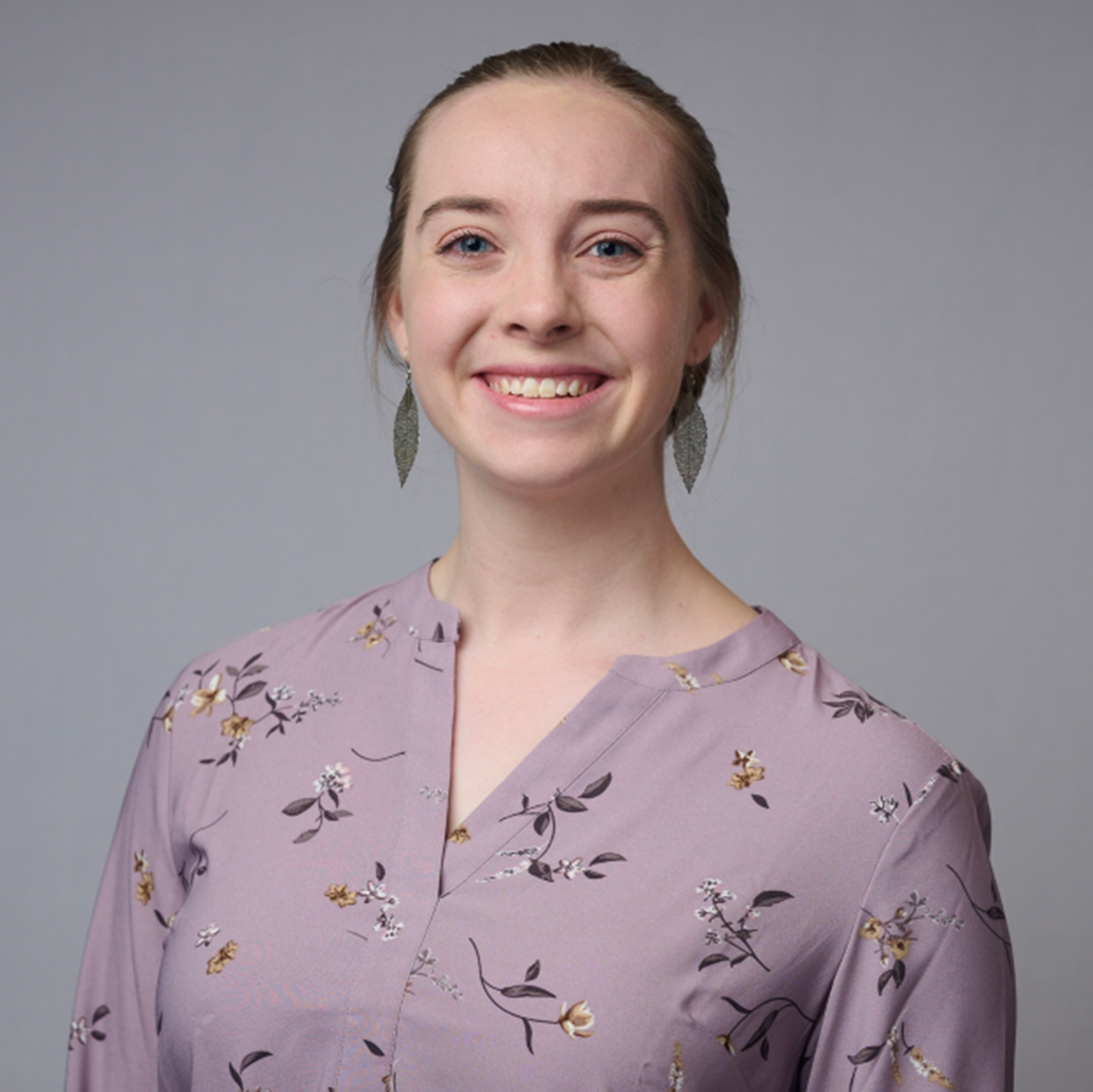 A person with dark brown hair tied behind their head wearing a pink floral shirt and f