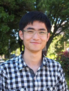 A person with short black hair and clear-framed glasses wearing a black plaid shirt smiling at the camera